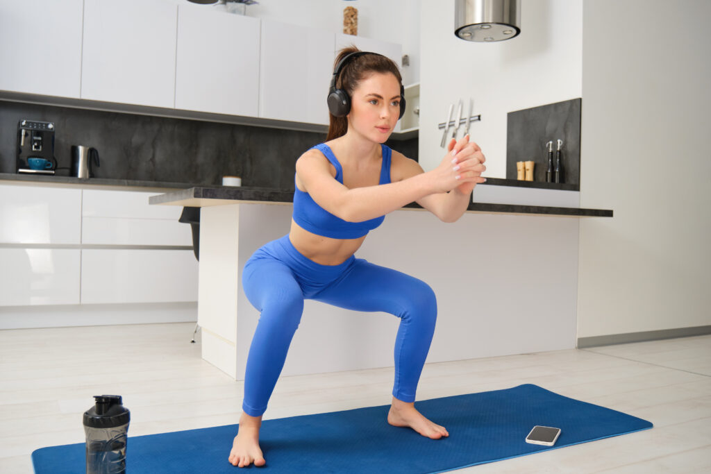 Fitness woman doing squats at home gym workout to build lower body strength, burn calories, and improve overall fitness
